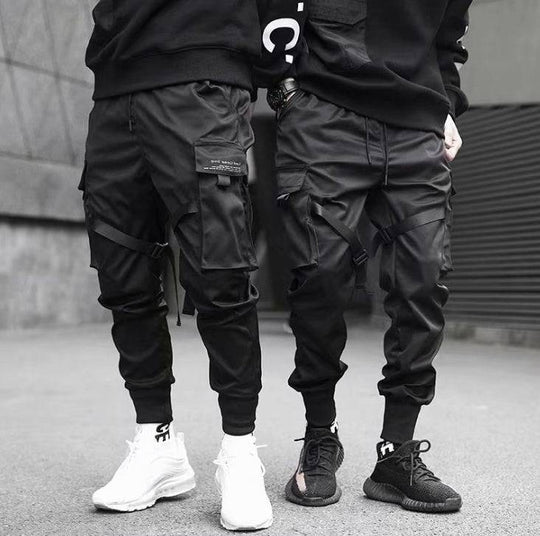 Men's cargo jogger pants in black with multiple pockets and ribbon details, styled for streetwear and hip hop fashion.