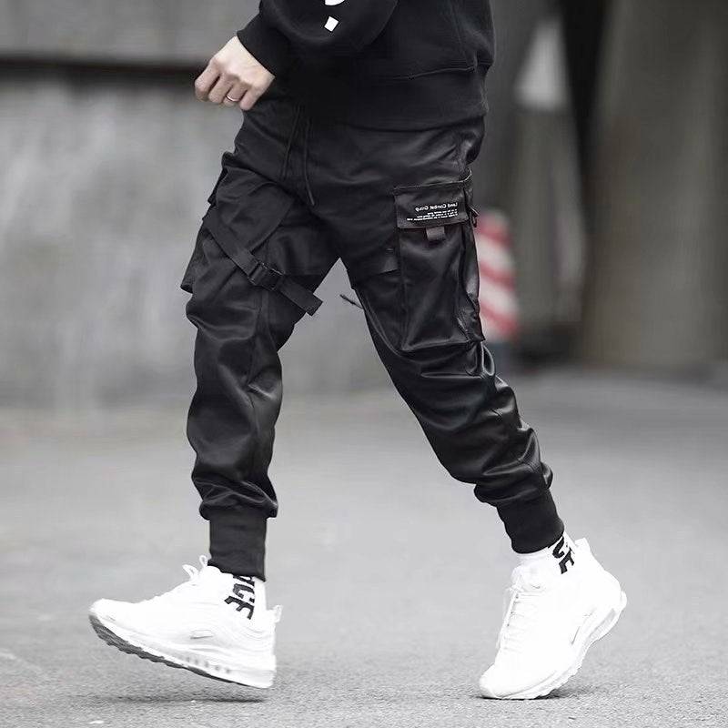 Black cotton cargo jogger pants for men with streetwear-inspired design, shown in motion with white sneakers and ribbed cuffs.