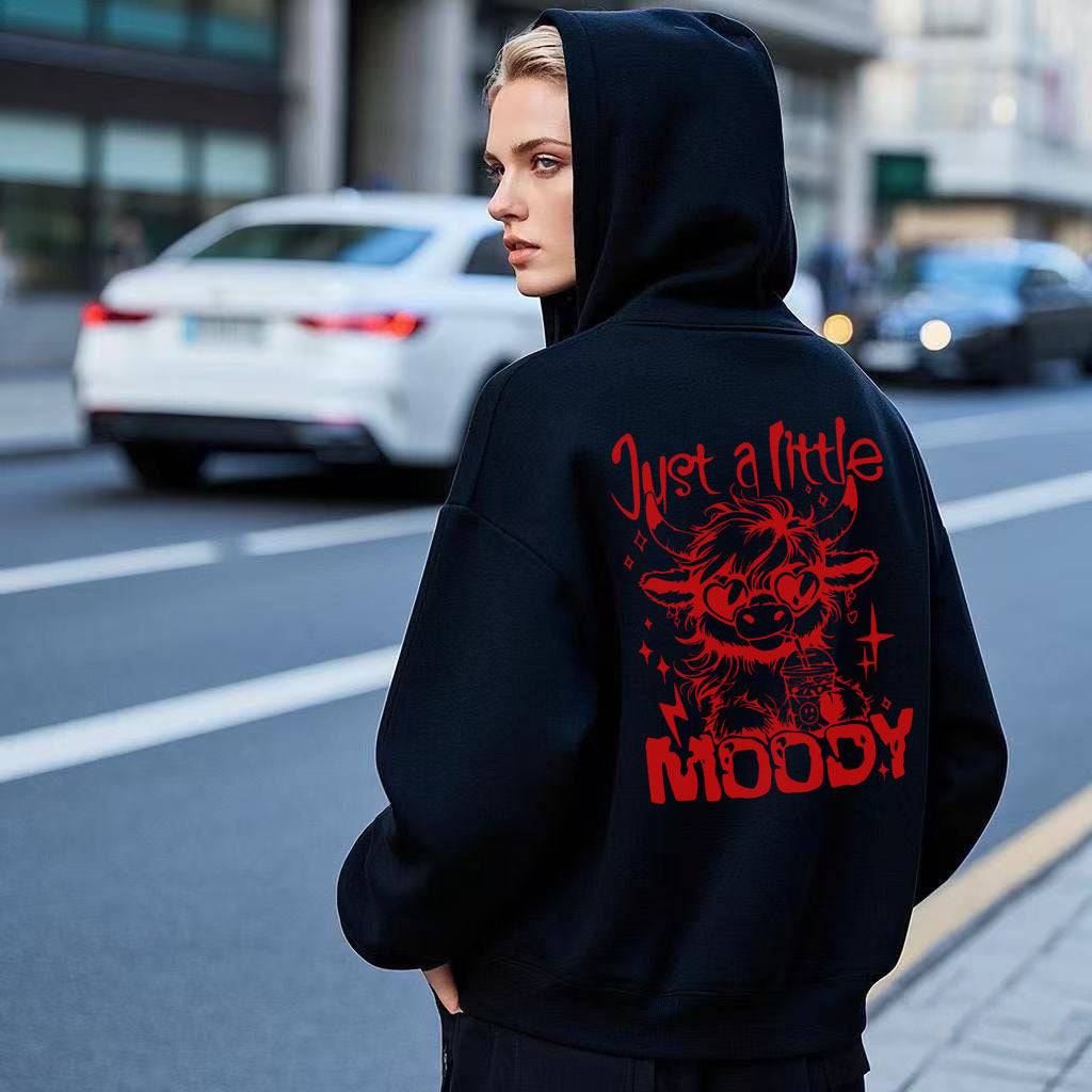 Black hoodie for men and women with red 'Just a Little Moody' cow print, showcasing trendy streetwear style.