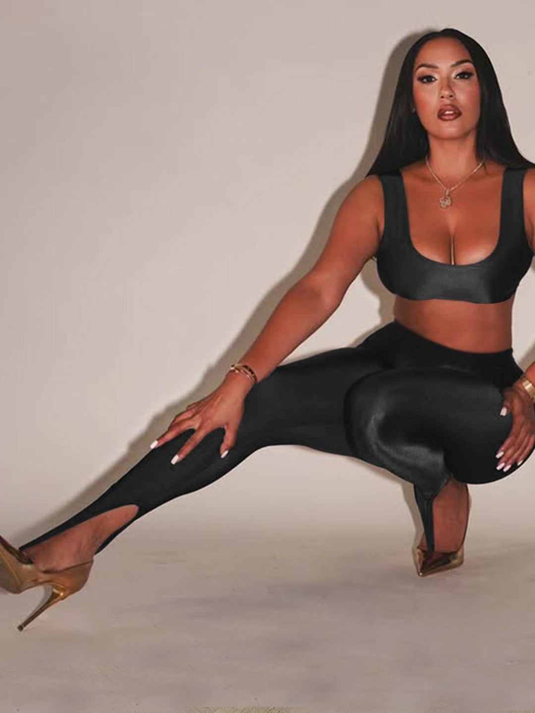 Front Step Shiny Leggings - Slim Fit Nylon Trousers in black, high-gloss finish with stirrup hem, styled with crop top and gold heels.